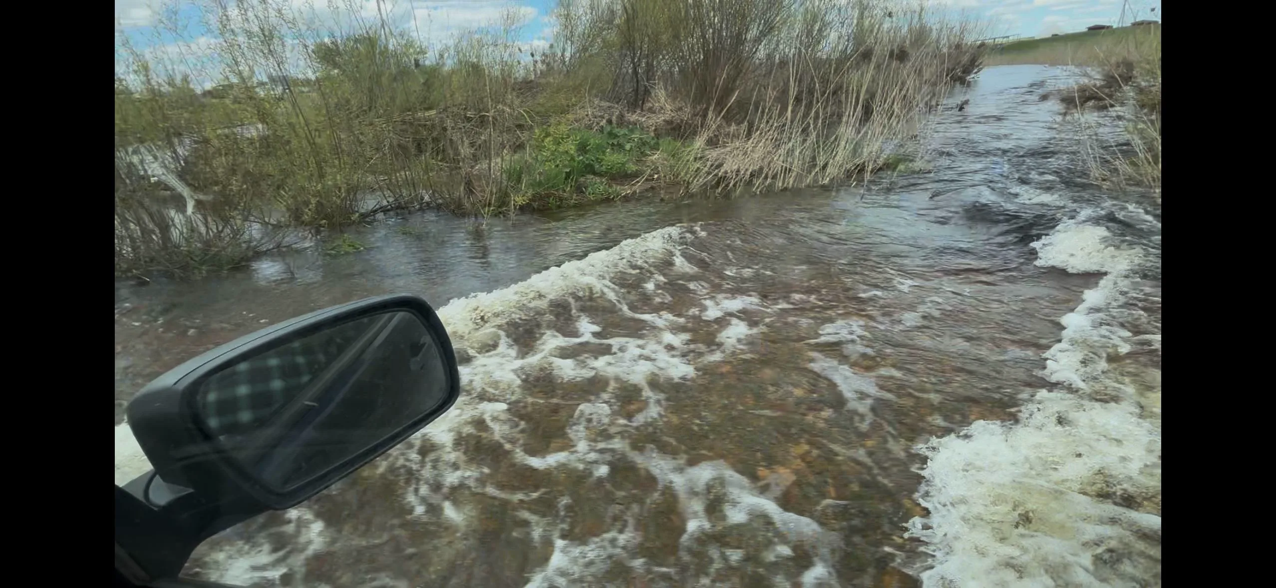 Вода идёт через дорогу — брод через разлившуюся Караганку из окна машины